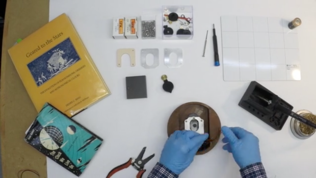 A top down view of a desk with a partially assembled clock and several time related books, parts and tools. 