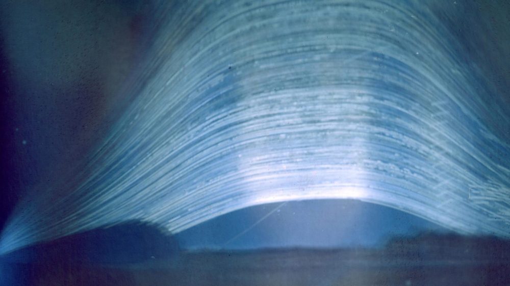 Curved streaks across a blue background represent the path of the sun in the sky over a multi-year photographic exposure. 