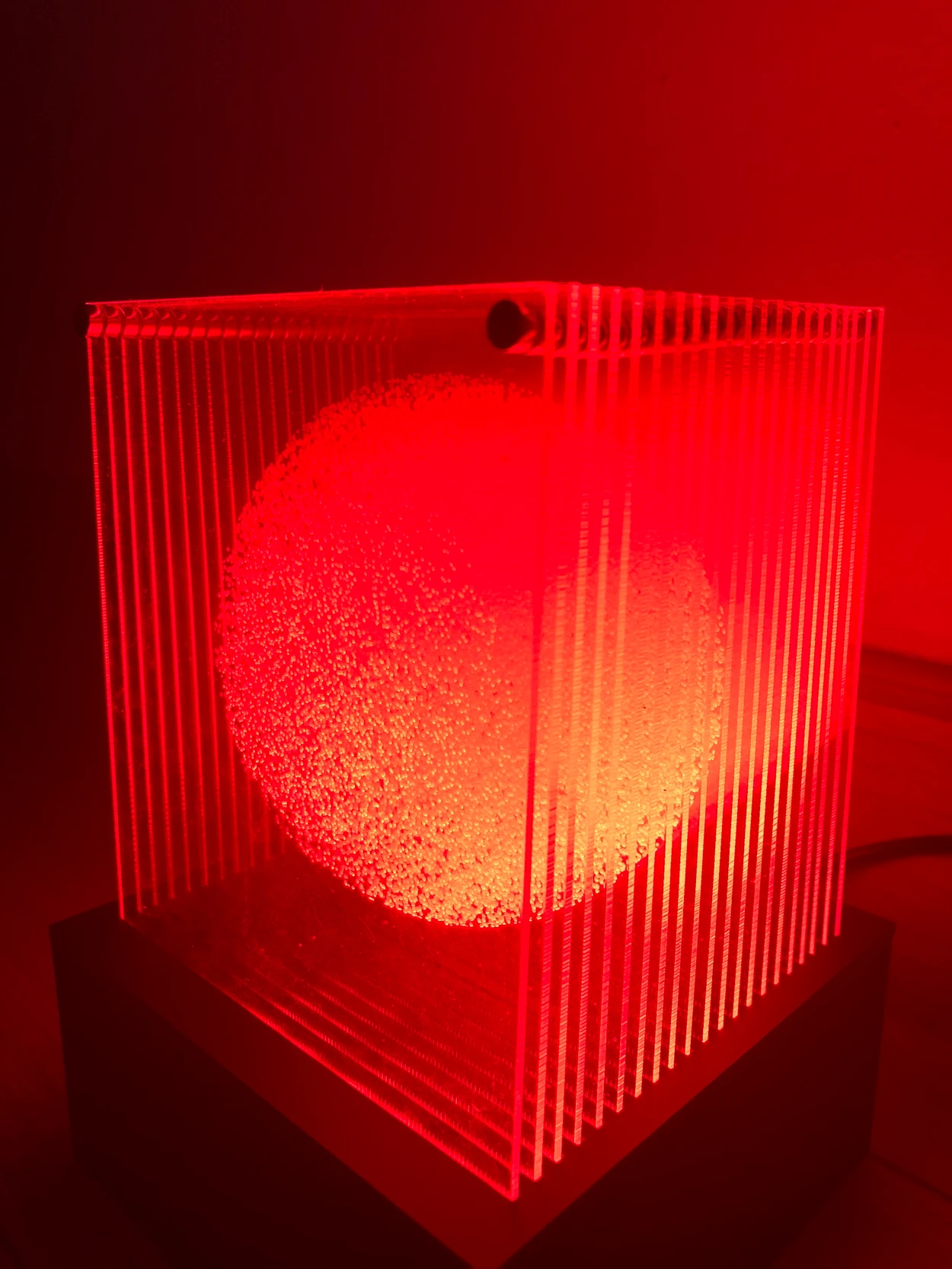 A glowing red orb embedded in parallel sheets of translucent acrylic.