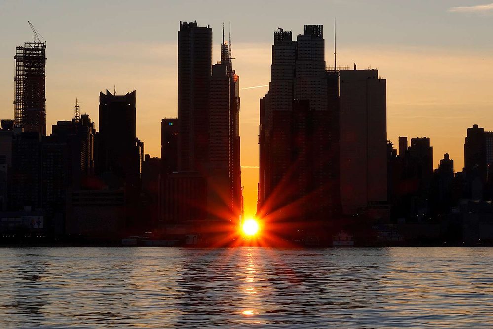 The sun sets directly between manhattan buildings